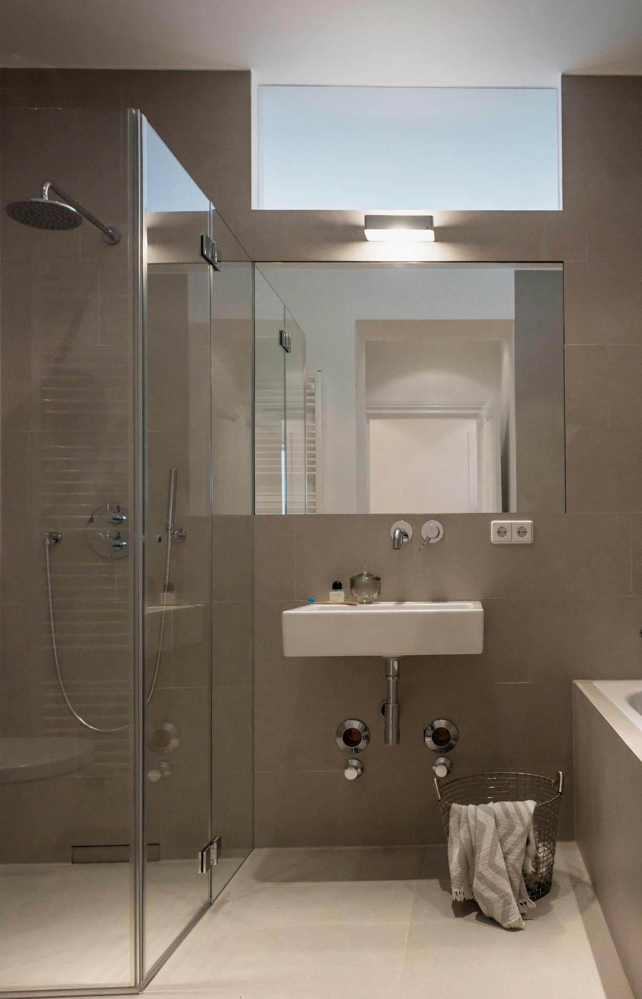 The image features a modern, clean bathroom with a large glass shower stall and a white sink. The shower stall is located next to the sink, and the sink is placed on a countertop. The bathroom appears to be well-lit, with a window providing natural light.

In addition to the sink and shower stall, there are two bottles placed near the sink, possibly containing toiletries or cleaning supplies. A towel is also visible on the countertop, likely for drying after using the bathroom.