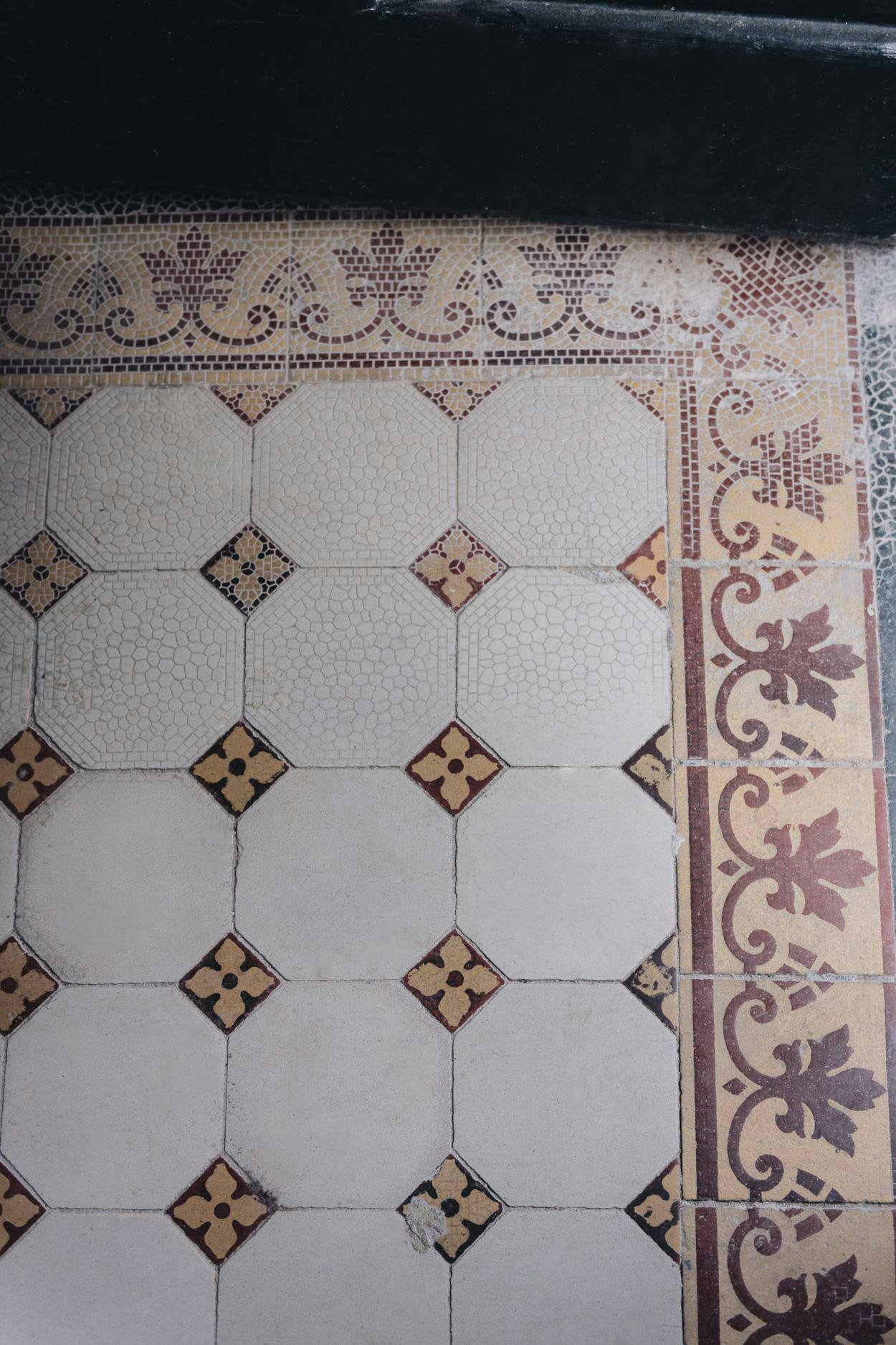 The image features a white and brown tile floor with a patterned design. The floor is covered in a variety of tiles, creating a visually appealing and unique appearance. The tiles are arranged in a pattern, with some tiles placed closer to the edges and others in the middle of the floor. The overall design of the tiles adds a sense of depth and texture to the floor, making it an interesting and eye-catching feature in the room.