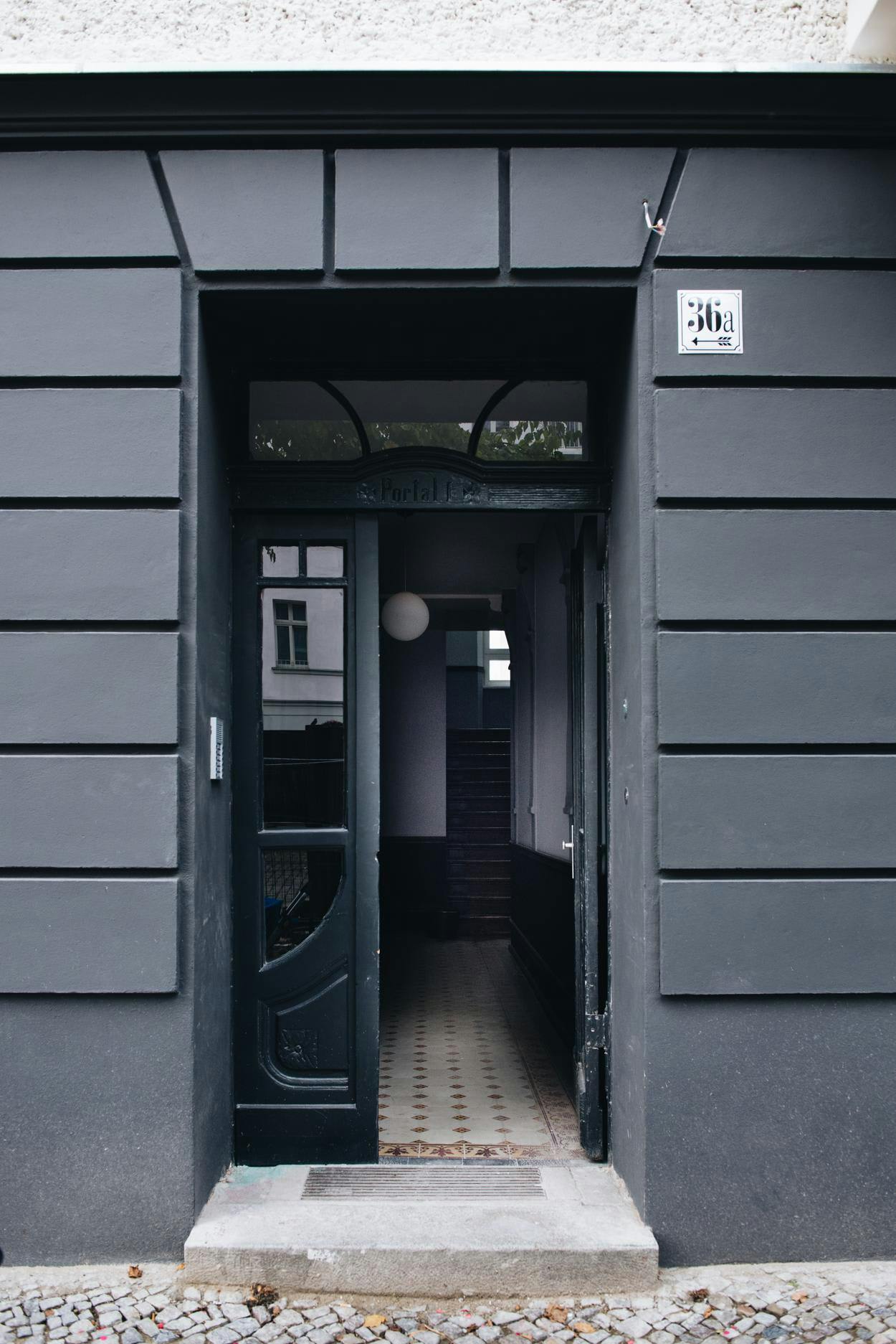 The image features a large, dark building with a black doorway and a sign on the side. The doorway is open, revealing a small, dark room inside. The room appears to be a storage area, as there is a small, dark room with a doorway and a sign on the side. The sign is located near the top of the doorway, and the room appears to be empty.

The building is situated next to a sidewalk, and there is a bench nearby, possibly for people to sit and rest. The scene conveys a sense of a quiet, empty space within the building.