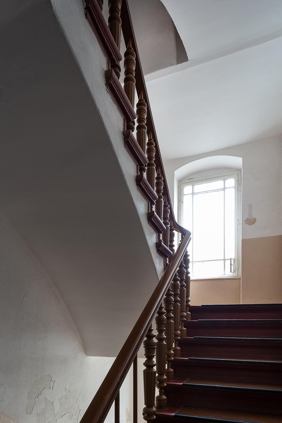 The image features a staircase with a black railing, leading up to a window. The staircase is situated in a hallway, and the window is located above the stairs. The staircase appears to be in a dark room, possibly a basement or a dark hallway. The presence of the window above the stairs suggests that the room could be a living space or a bedroom.