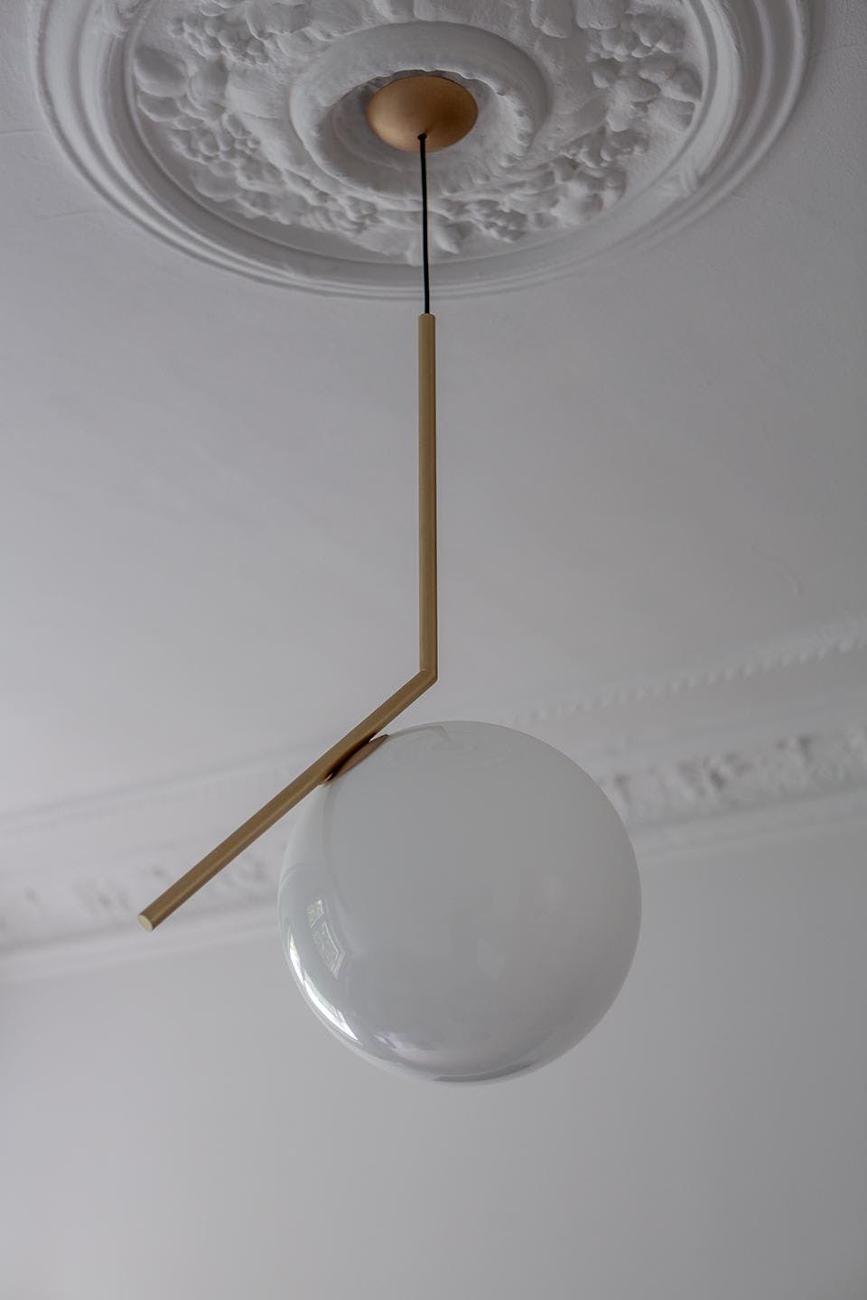 The image features a white ceiling with a large, round, and white light fixture hanging from it. The light fixture is suspended from a wooden pole, and it appears to be a chandelier. The ceiling is decorated with a white ceiling fan, which is also suspended from the ceiling. The fan is positioned towards the top of the ceiling, adding a touch of elegance and style to the room.