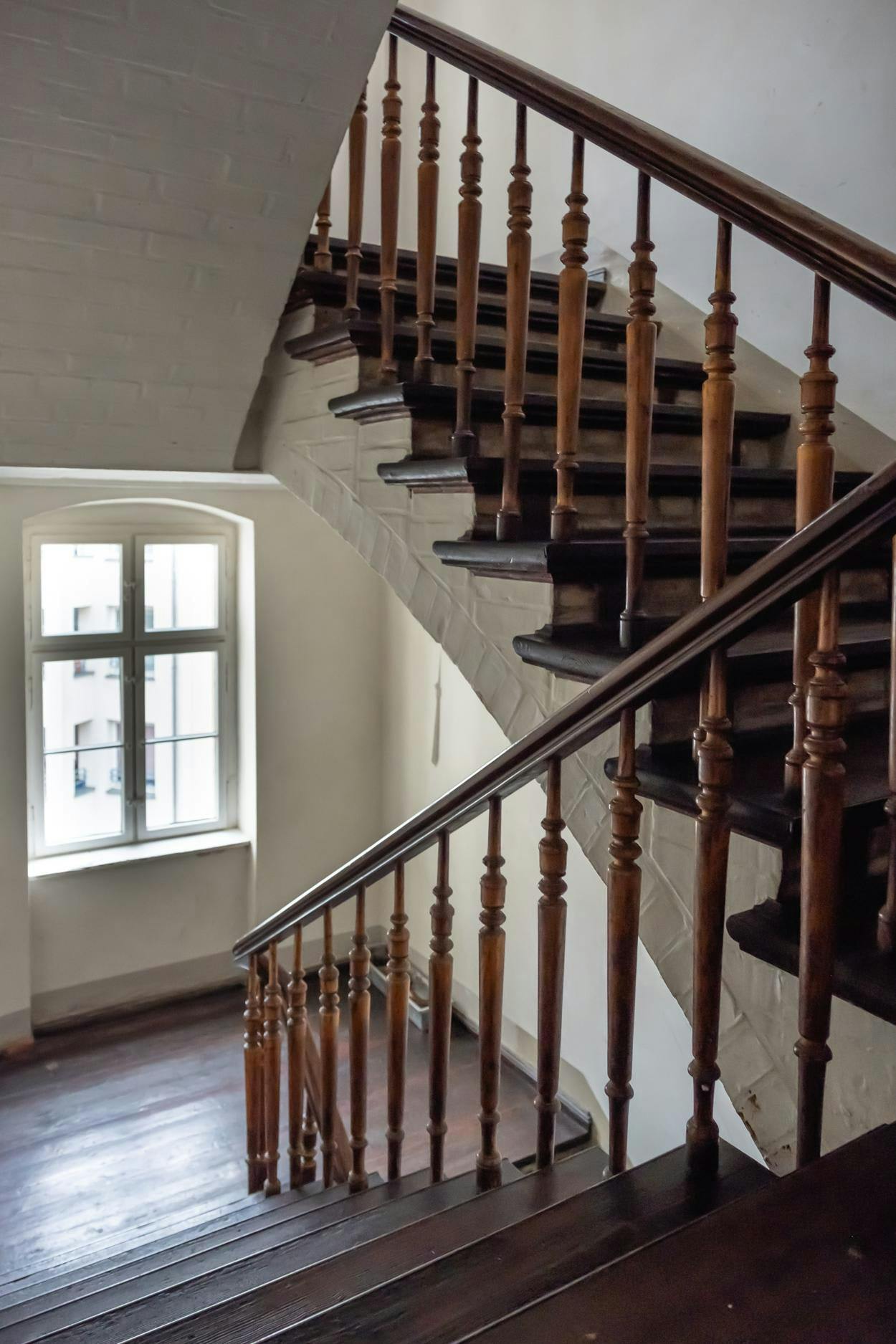 The image features a wooden staircase with a metal railing, located in a house with a window.