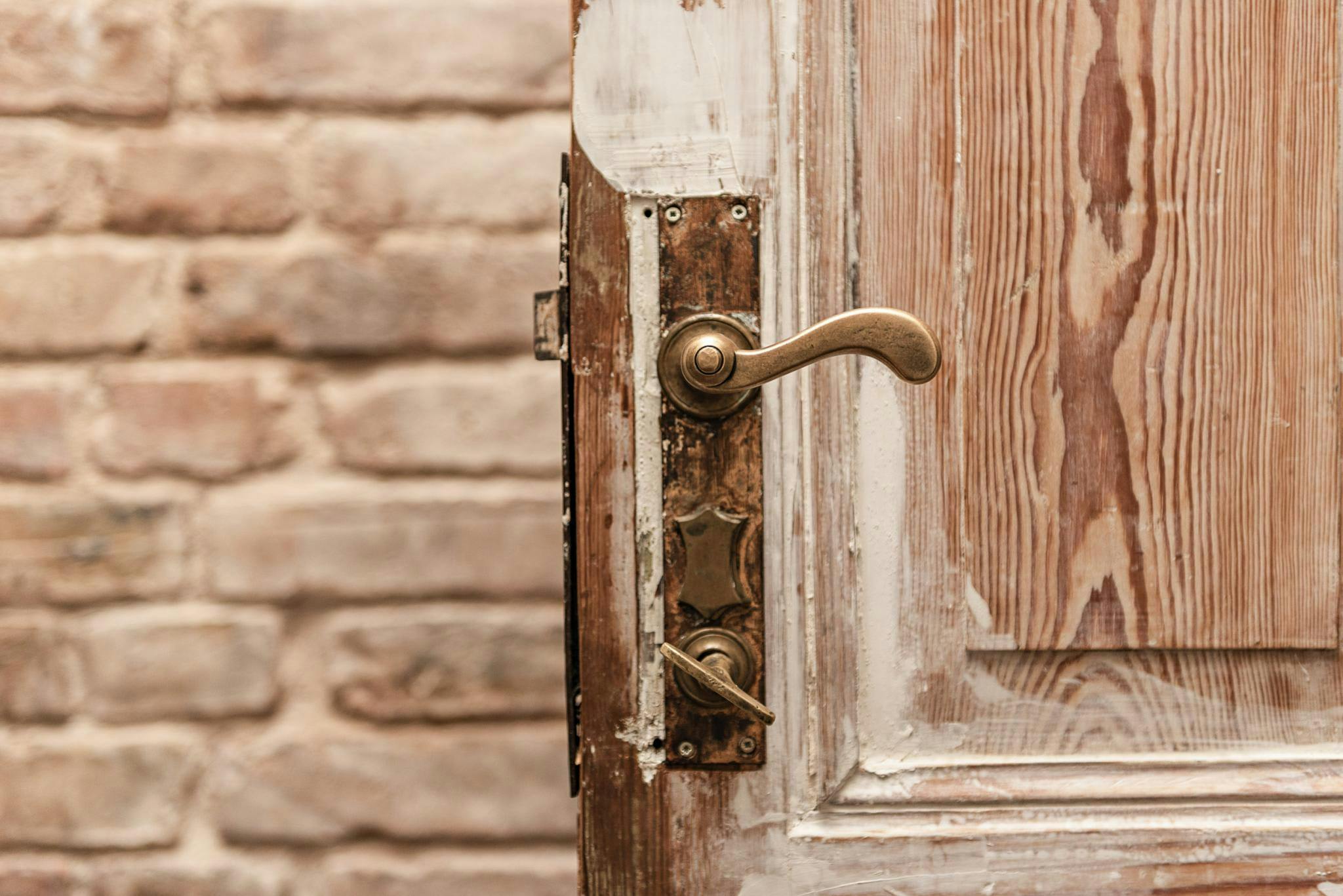 The image features a wooden door with a brass handle, which is open and slightly ajar, revealing a brick wall behind it.