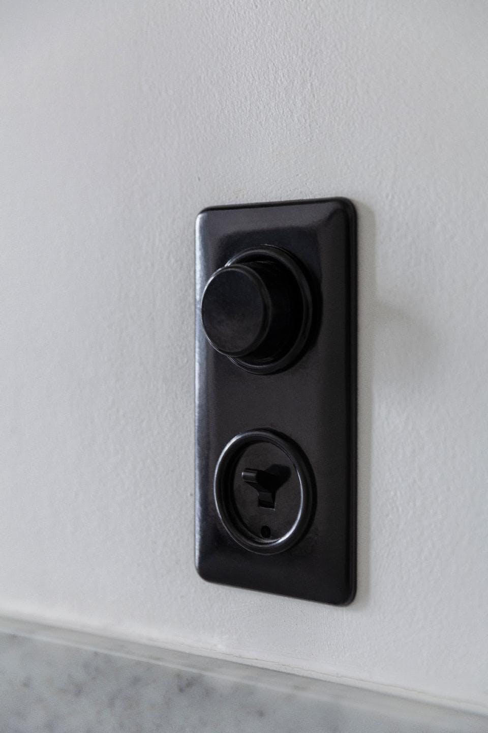 A black and silver electronic device, possibly a remote control or a speaker, is mounted on a white wall.