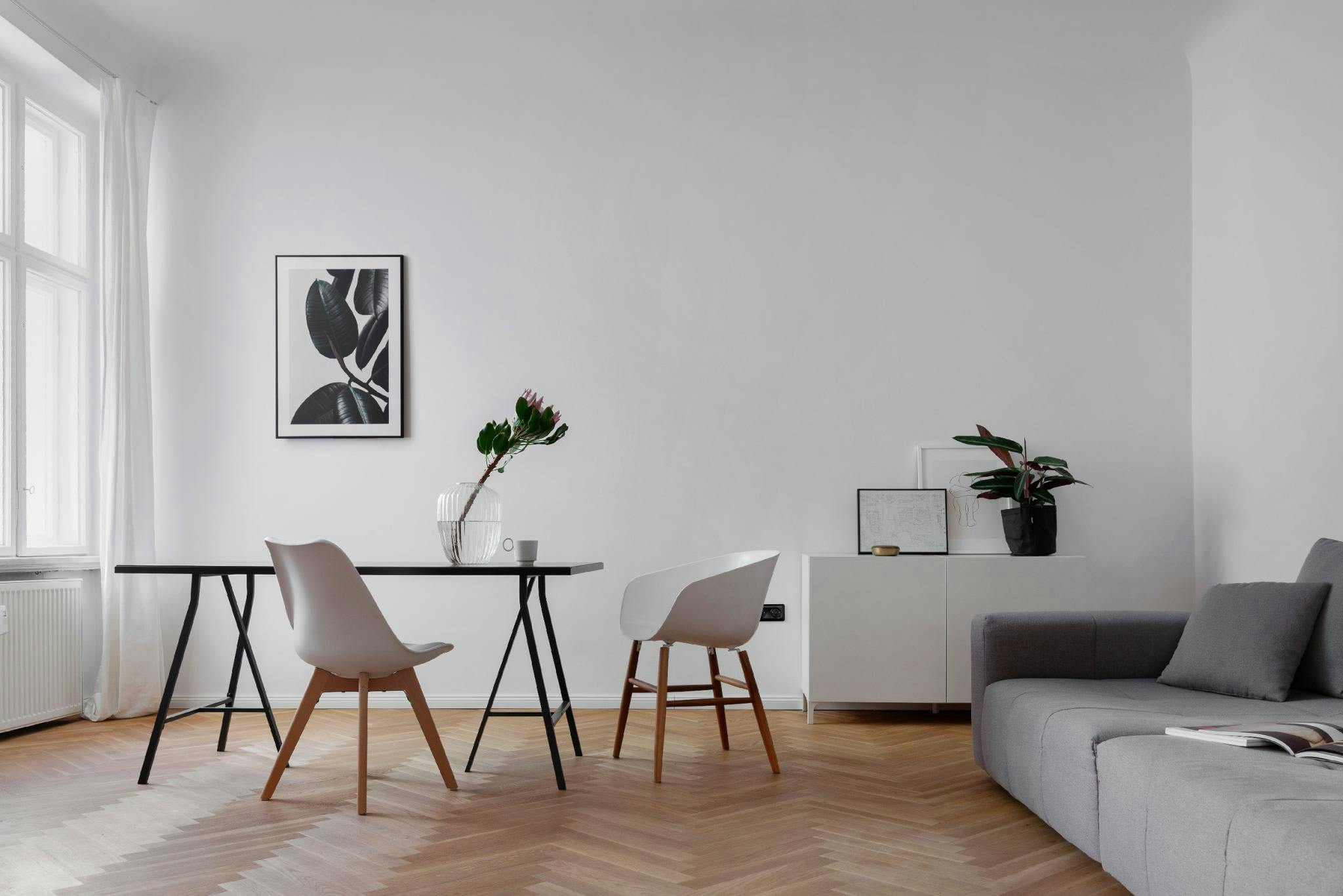 The image features a modern, white living room with a dining table and chairs, a couch, a potted plant, and a vase.