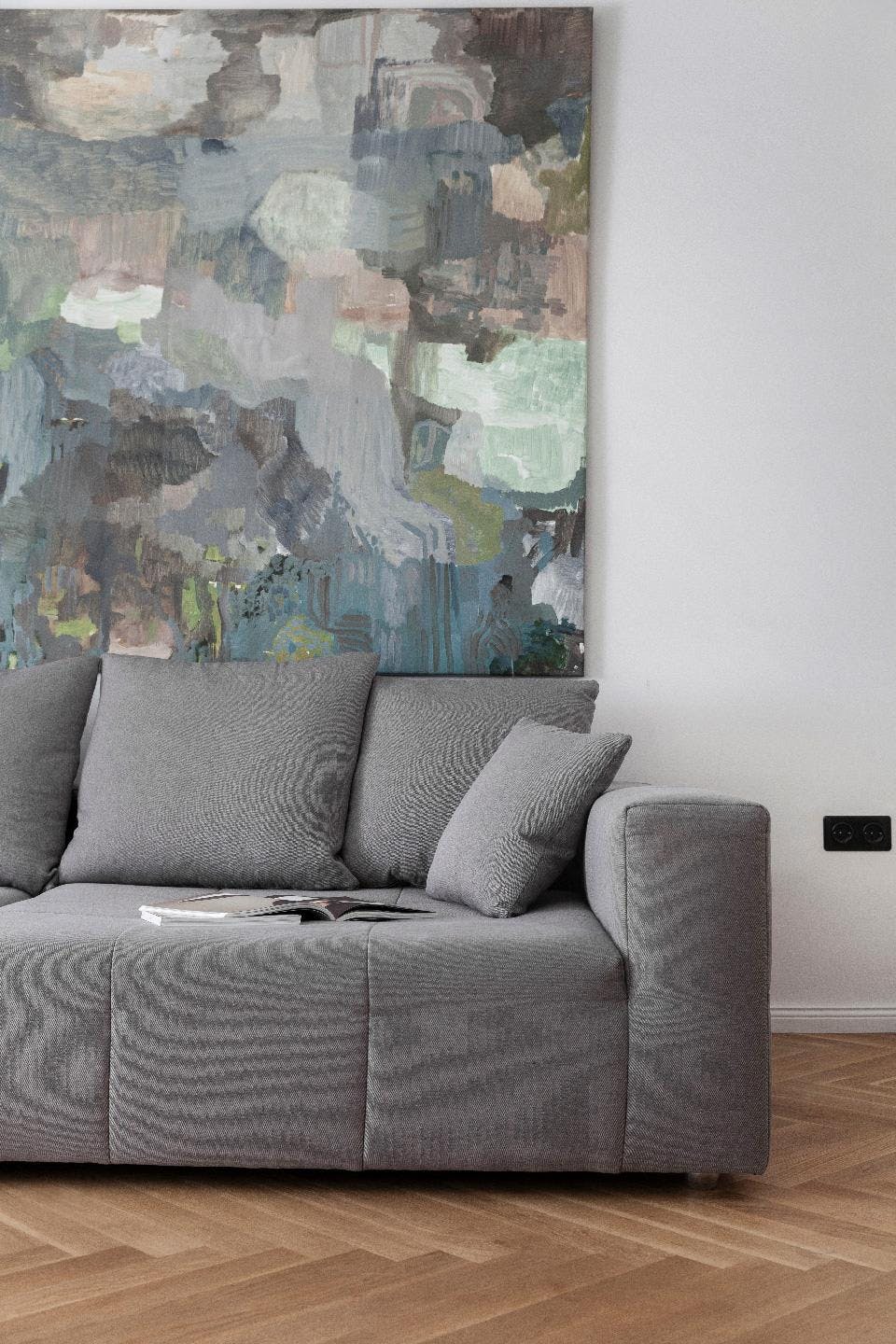 A gray couch is placed in a living room with a painting on the wall above it.