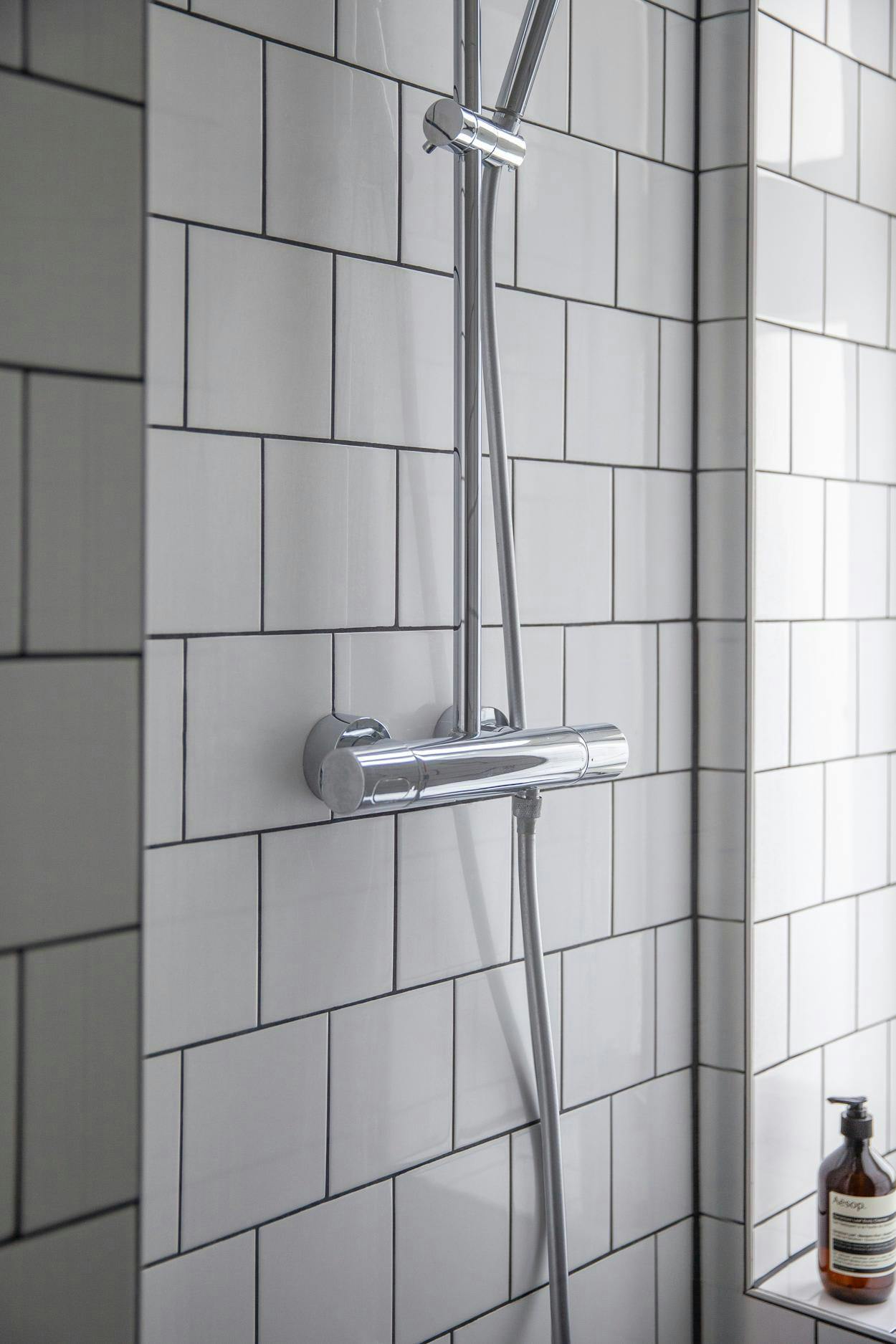 The image features a modern bathroom with a shower stall, a glass shower head, and a tiled wall.