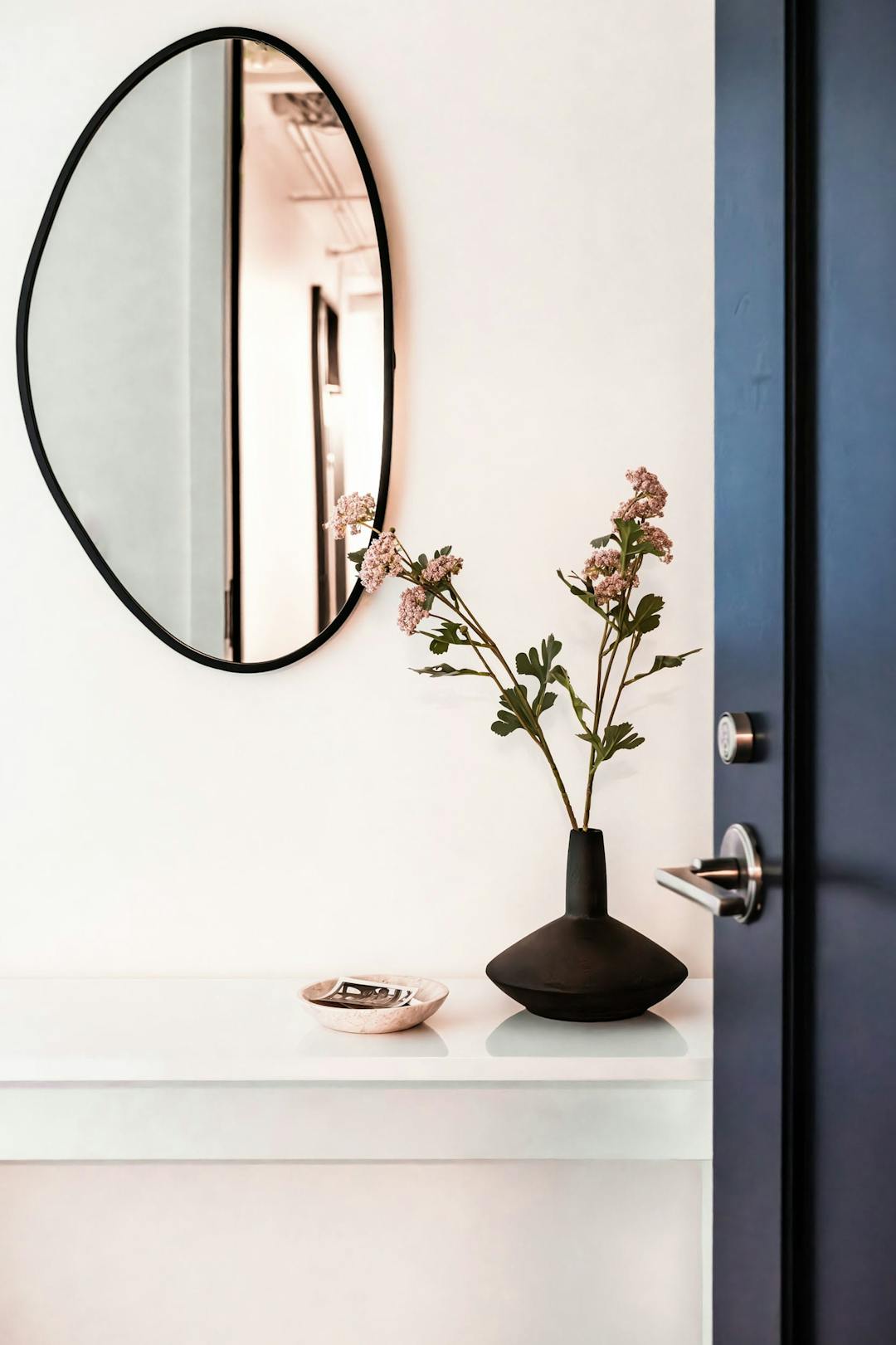 a vase with flowers sitting on a white table in front of a mirror on the wall of a room