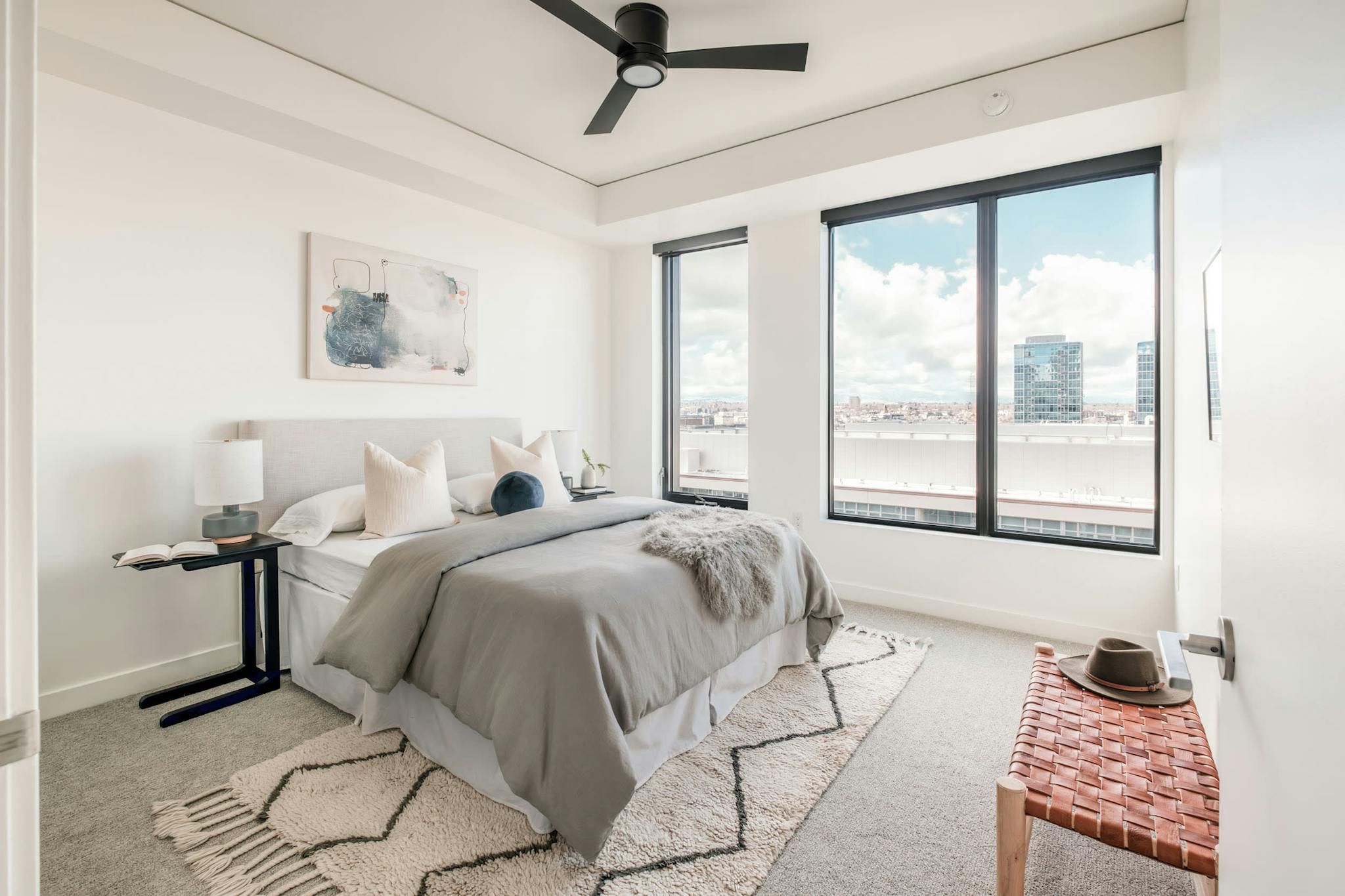 a bedroom with a large bed and a ceiling fan in the corner of the room with a view of the city outside the window