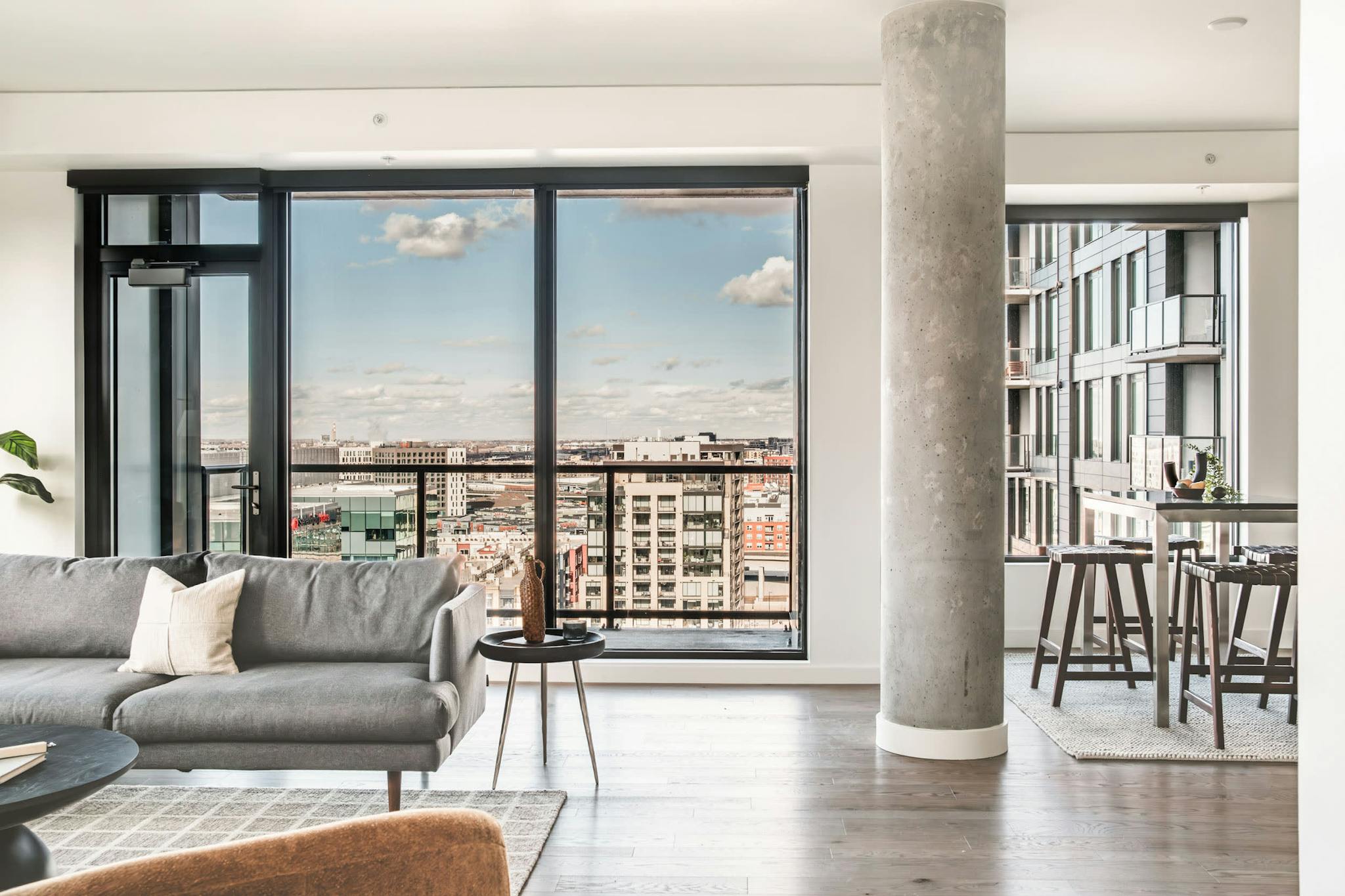 a living room filled with furniture next to a tall glass wall with a view of a city outside of it