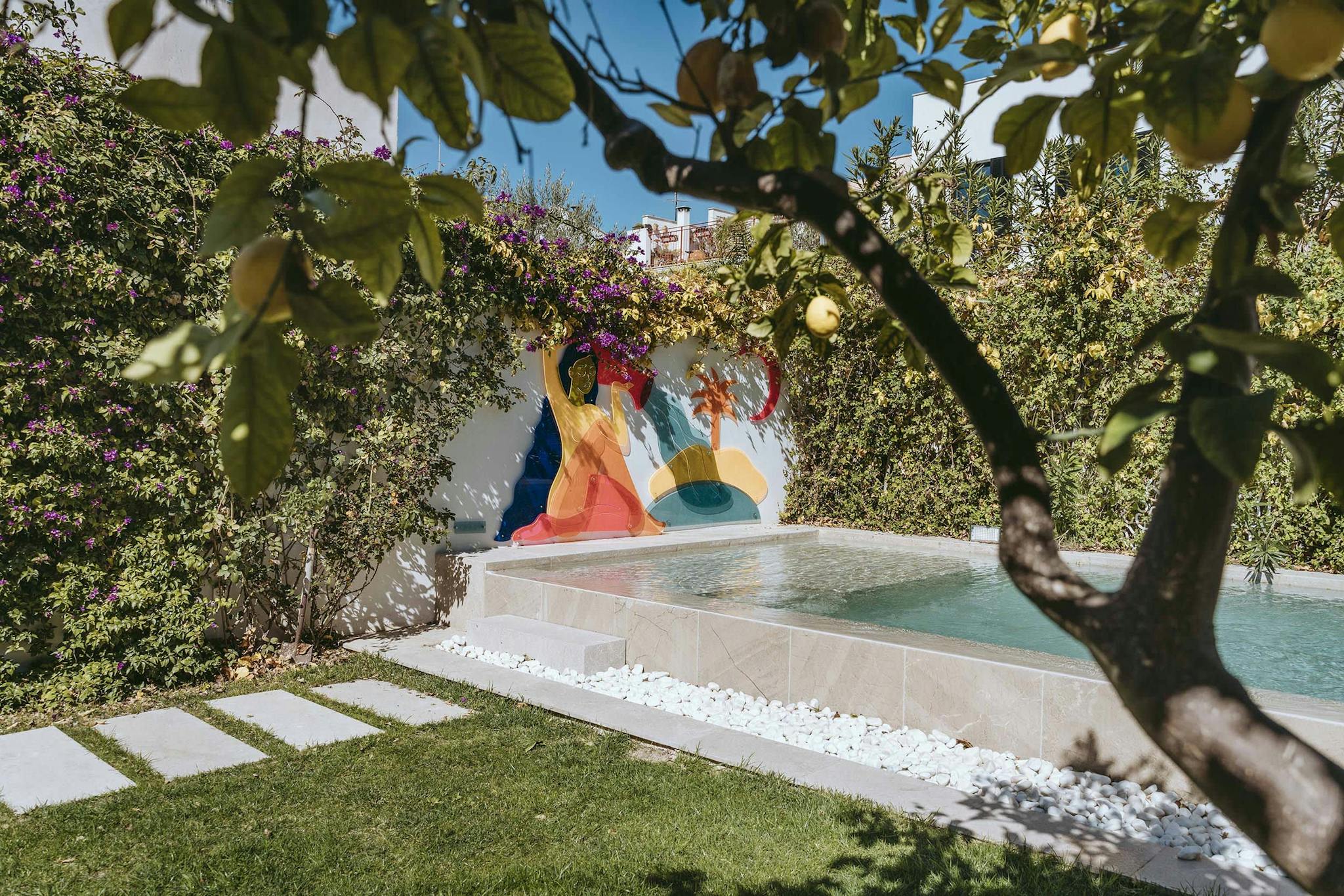 The image features a large, colorful swimming pool in a backyard, surrounded by a lush green lawn and trees. The pool is filled with water and has a colorful, rainbow-colored umbrella floating in the pool.