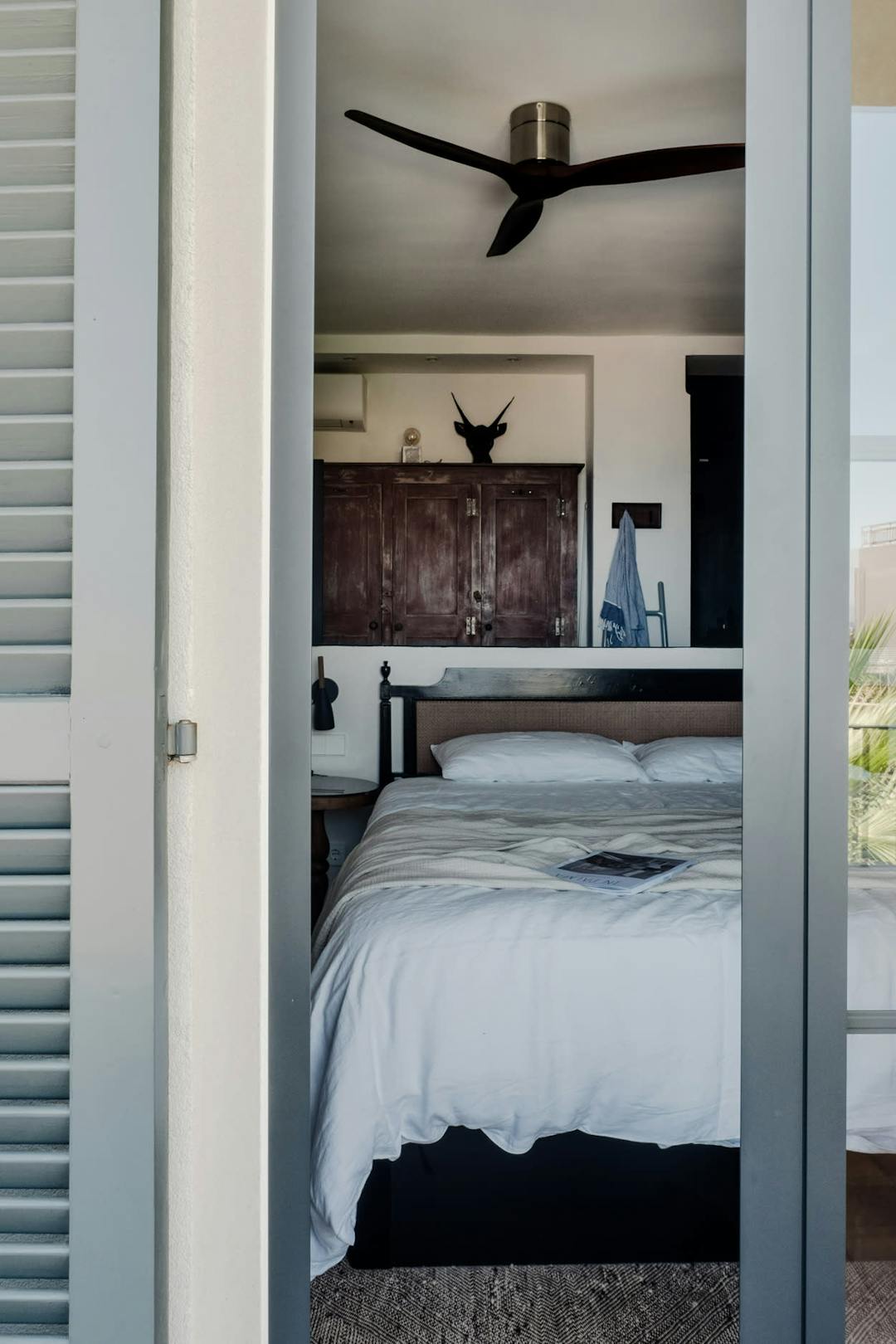 The image features a bedroom with a neatly made bed, a ceiling fan, a window, and a door.